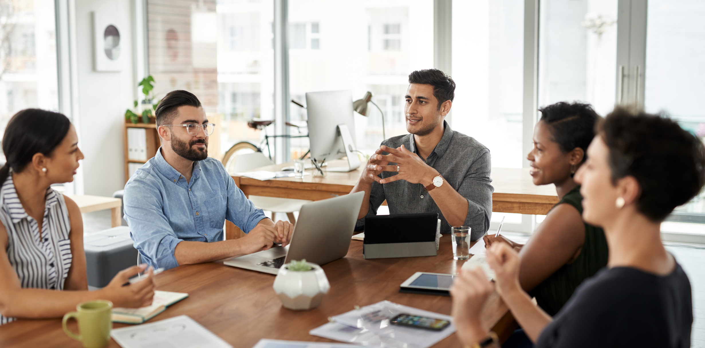 Group of colleagues talking at a conference table with computers in front of them